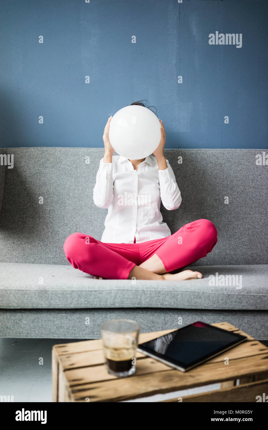 Donna seduta sul lettino nasconde il suo volto dietro una sfera bianca Foto Stock