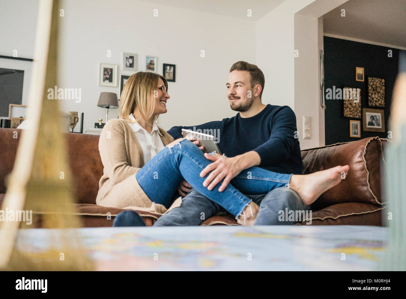 Sorridente giovane seduto sul divano di casa con la compressa Foto Stock