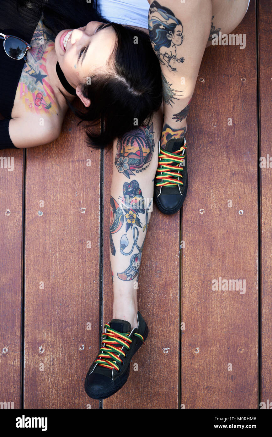 Dal dettaglio di cui sopra di tatuati gambe e amico di ragazza felice giacente sul piano di un ponte di legno. Foto Stock