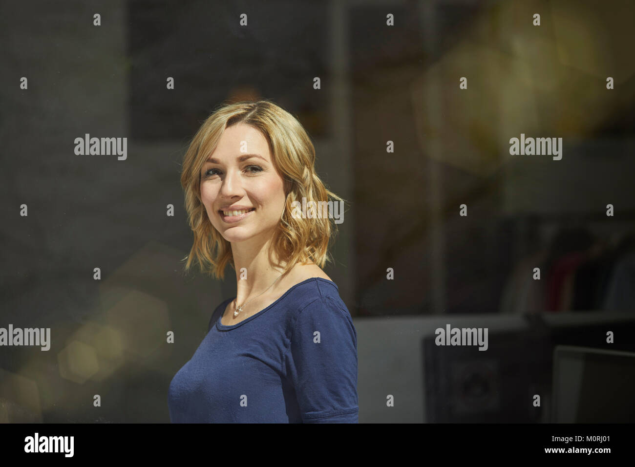 Ritratto di donna bionda dietro vetro, sorridente Foto Stock