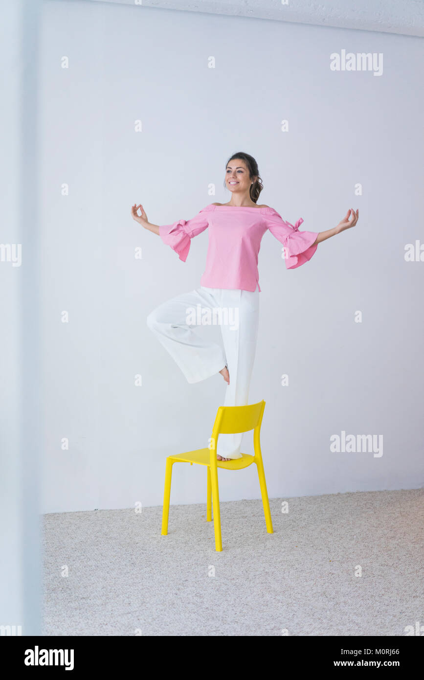 Felice giovane donna in piedi sulla sedia gialla facendo esercizi yoga Foto Stock