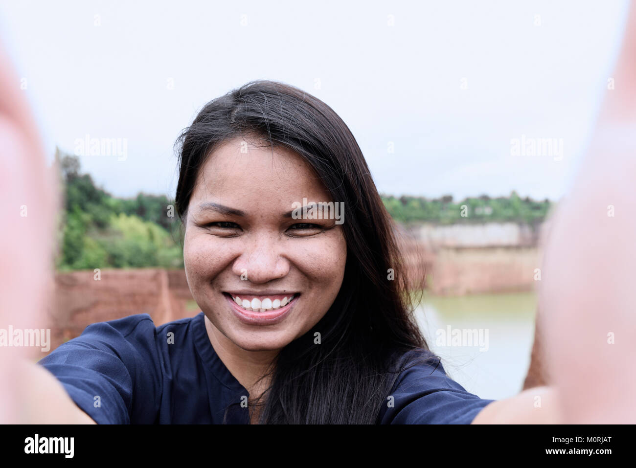 Bella donna asiatica prendendo un autoritratto con il suo telefono, sorridente alla fotocamera. Foto Stock