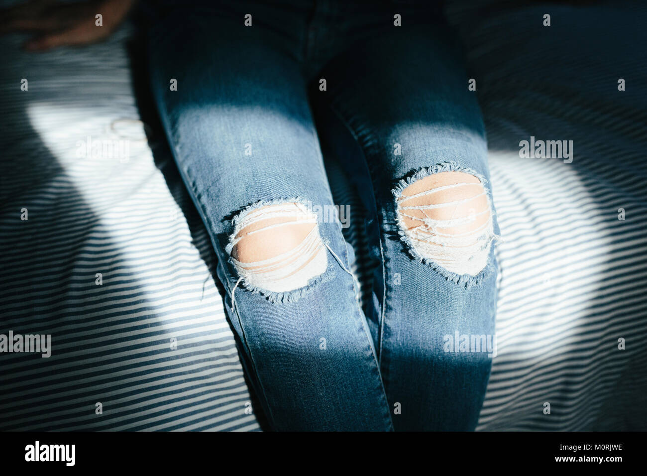 Close-up di donna seduta sul letto di casa che indossano jeans strappati Foto Stock