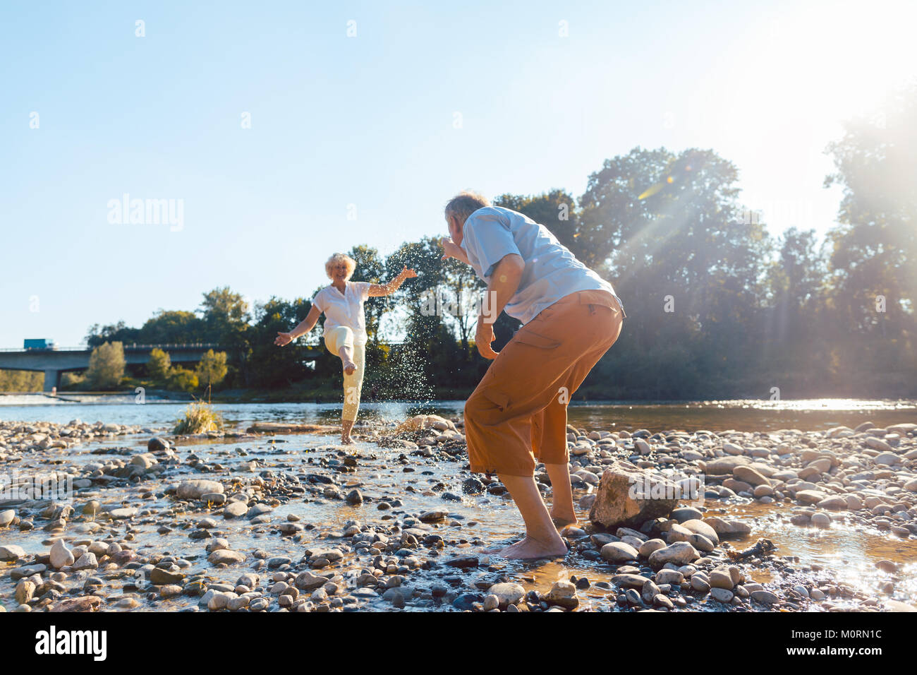 Divertente coppia senior giocando con acqua al fiume in una soleggiata d Foto Stock