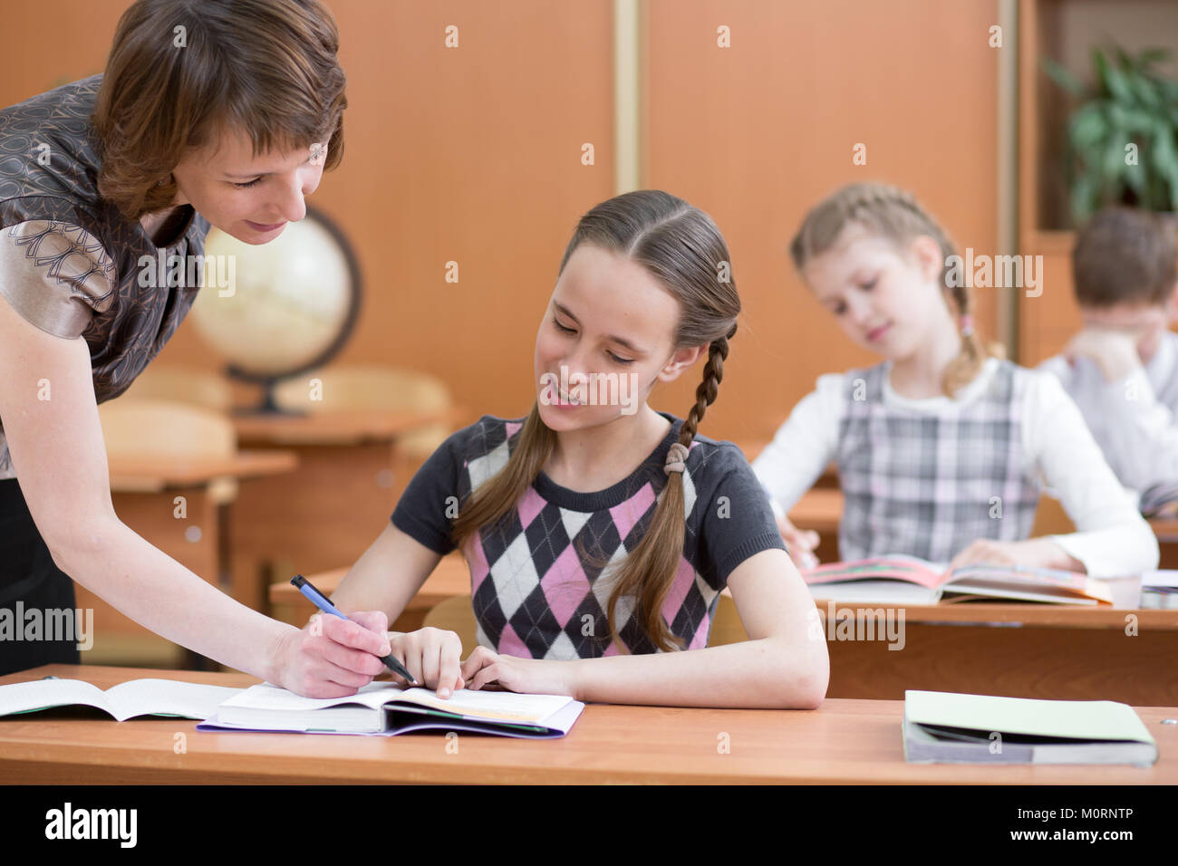 Schoolgirl sta studiando. A scuola i bambini lavorano a lezione. Docente di controllo del processo di apprendimento. Foto Stock