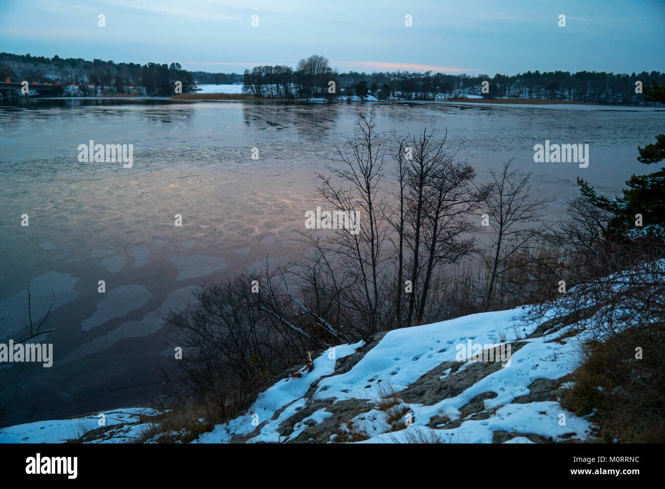 Vista lago con acque congelate preso da una costa rocciosa. Sull'altro lato del lago vi sono foreste e alcuni terreni agricoli. Foto Stock