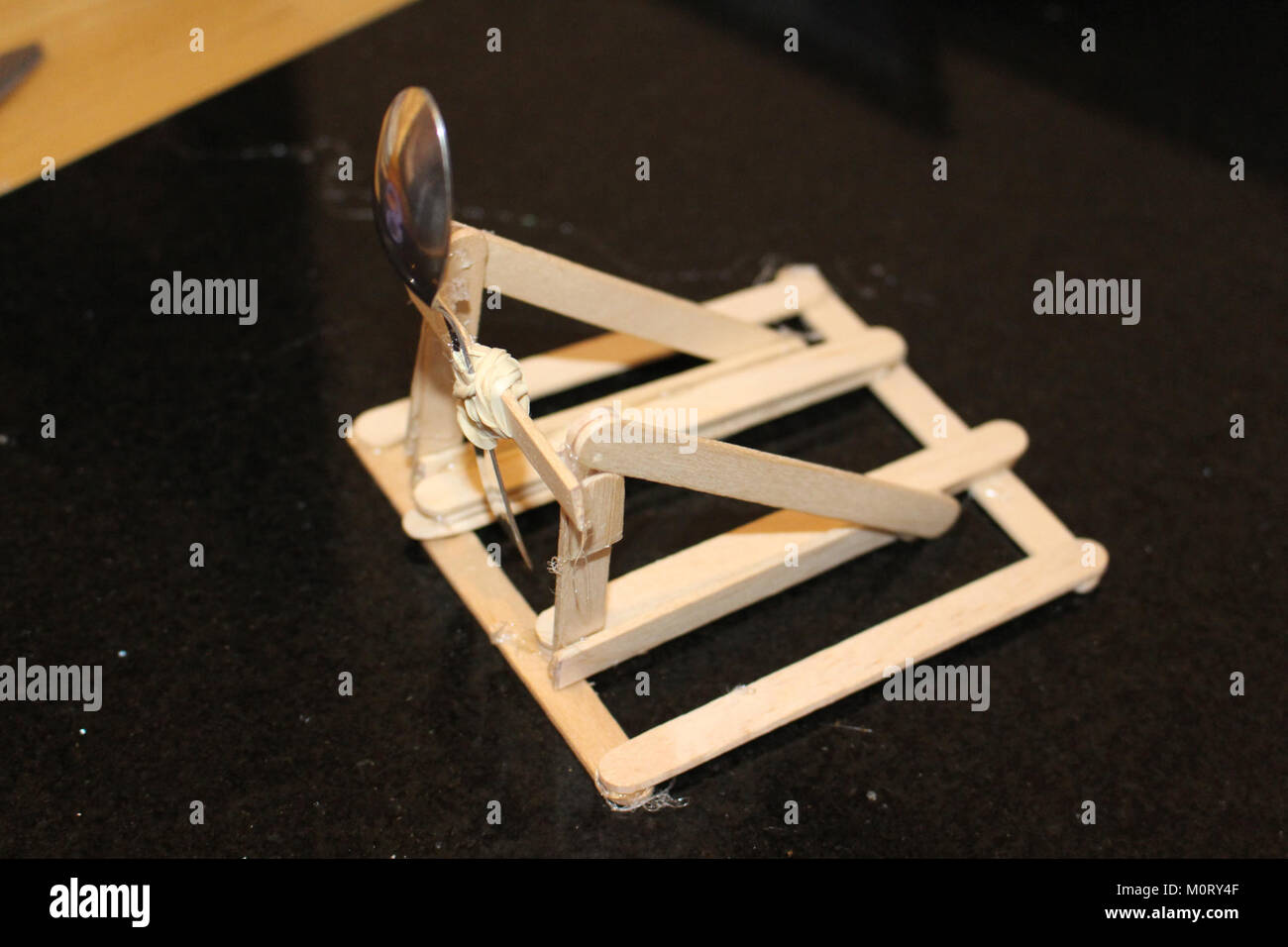 Questa semplice catapulta, costruita con bastoncini di artigianato, dimostra i principi di base della fisica. Utilizza la tensione per lanciare proiettili, fornendo uno strumento educativo per dimostrare meccanica e movimento. Foto Stock