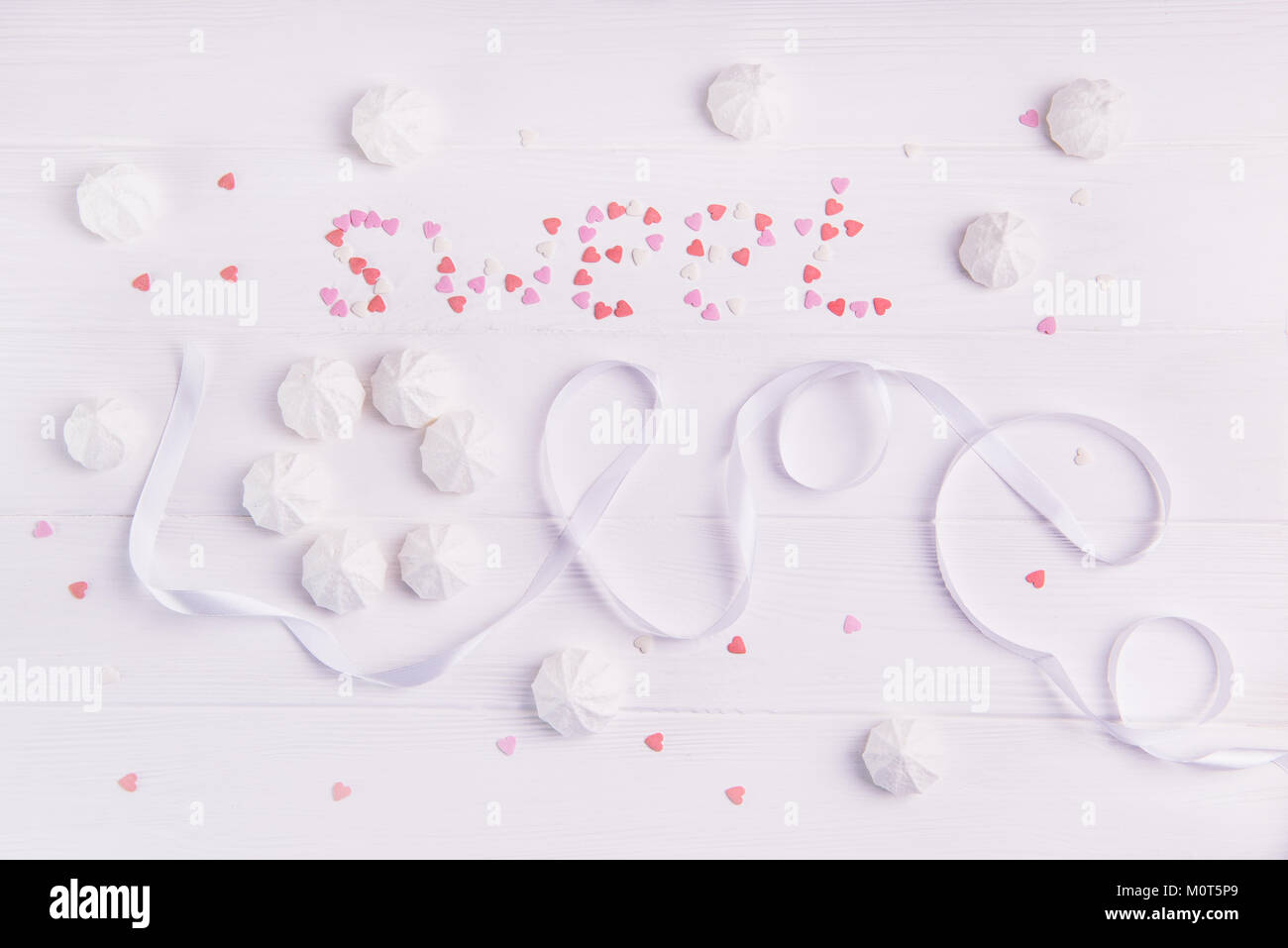Dolce amore scritte da nastro bianco, il merengue, dolciumi e caramelle multicolore a forma di cuore in bianco sullo sfondo di legno. Espressione di amore. Il giorno di San Valentino. Foto Stock