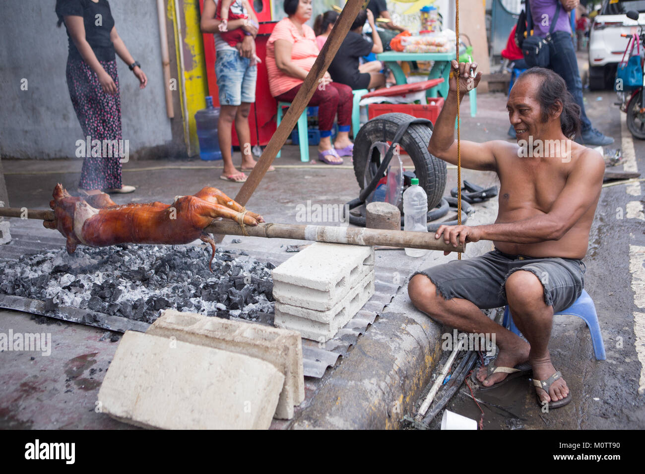 Un uomo arrosti allo spiedo un maiale noto come Lechon baboy nelle Filippine. Considerato come un cittadino piatto preferito. Foto Stock