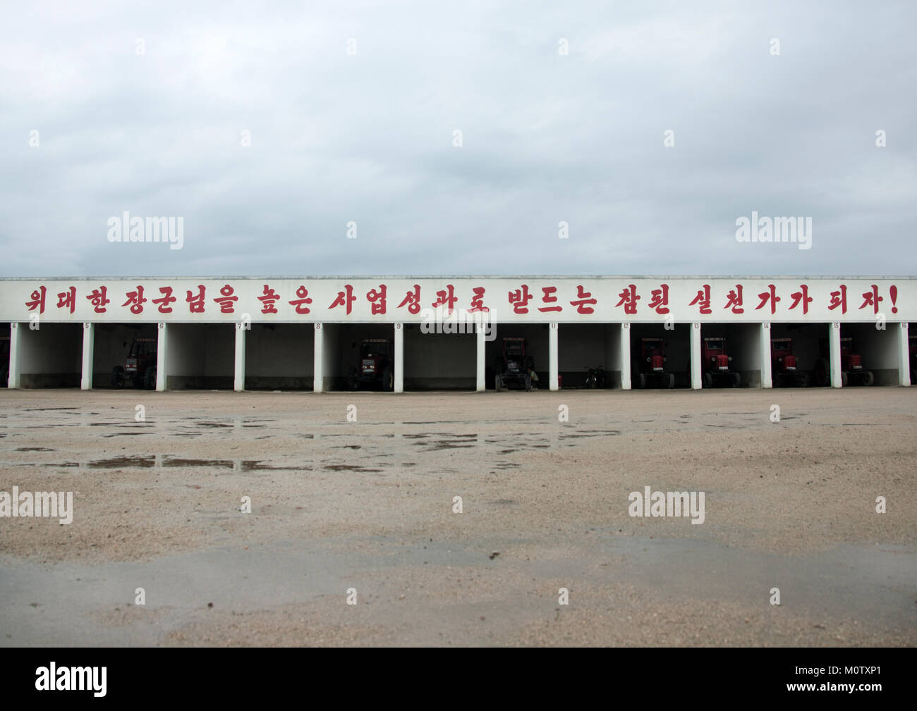 Lo spazio di archiviazione per i veicoli di fattoria con uno slogan sulla parte superiore, Sud Hamgyong Provincia, Hamhung, Corea del Nord Foto Stock