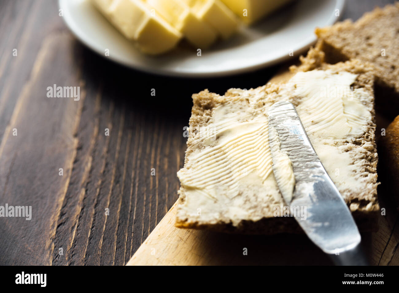 Un coltello diffusione di burro sul pane su sfondo di legno Foto Stock