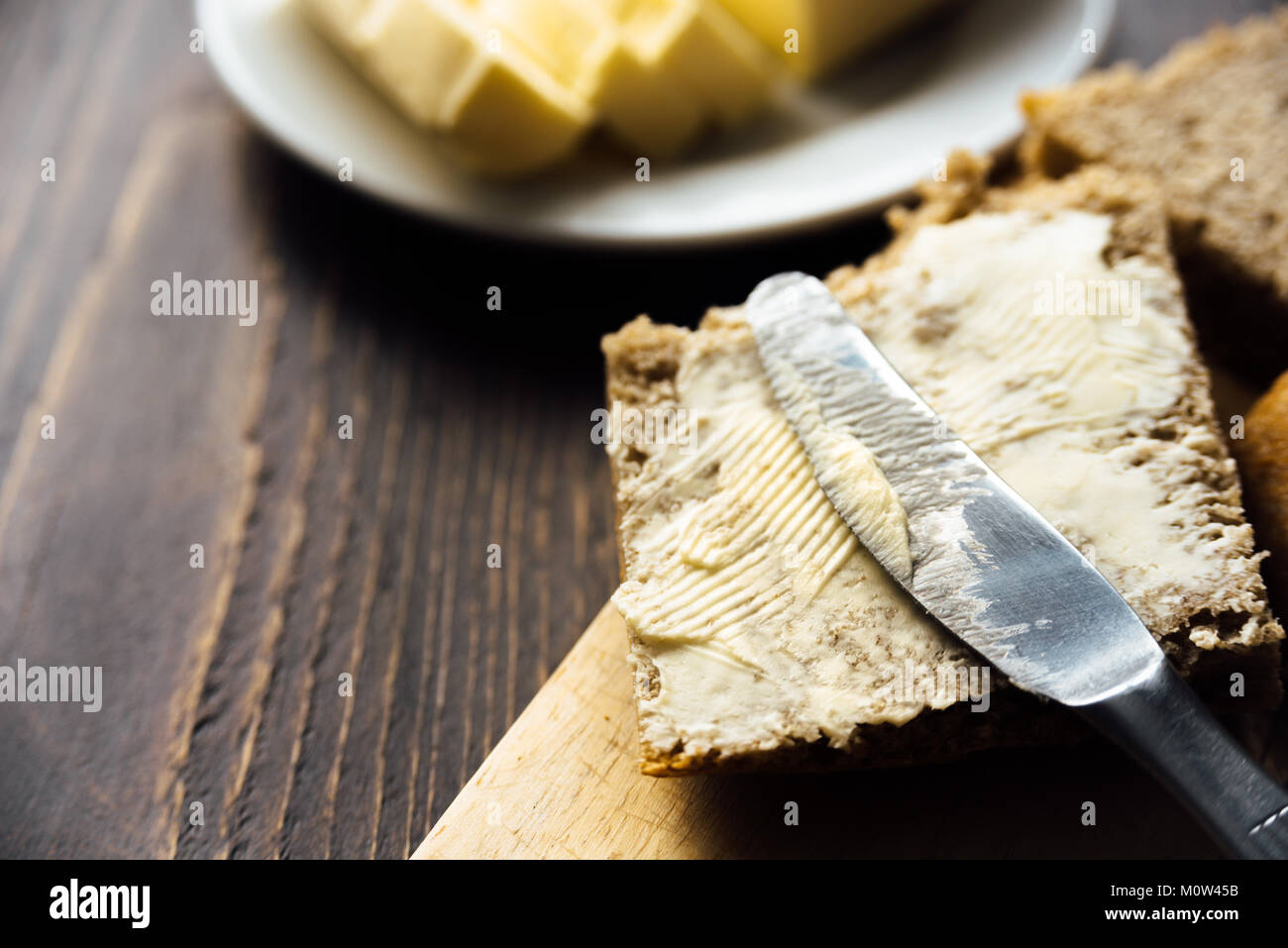 Un coltello diffusione di burro sul pane su sfondo di legno Foto Stock