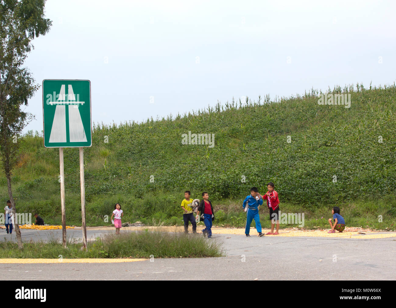 Corea del Nord i bambini a giocare davanti a un'autostrada entrance road sign in prossimità della zona demilitarizzata, Nord provincia Hwanghae, Panmunjom, Corea del Nord Foto Stock