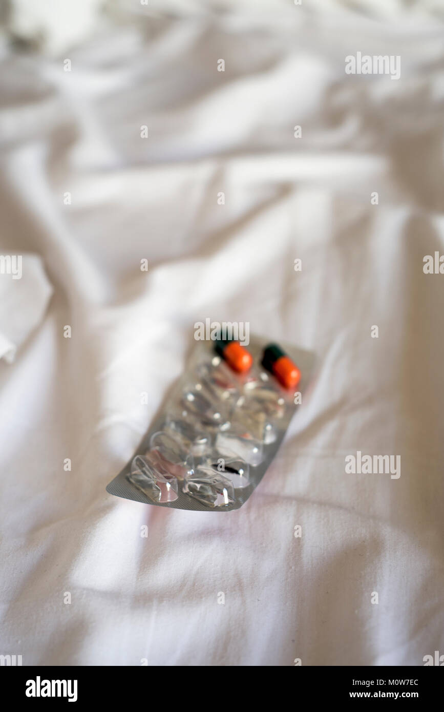 Un blister con due restanti pillole, sulle bianche lenzuola di un letto disfatto Foto Stock