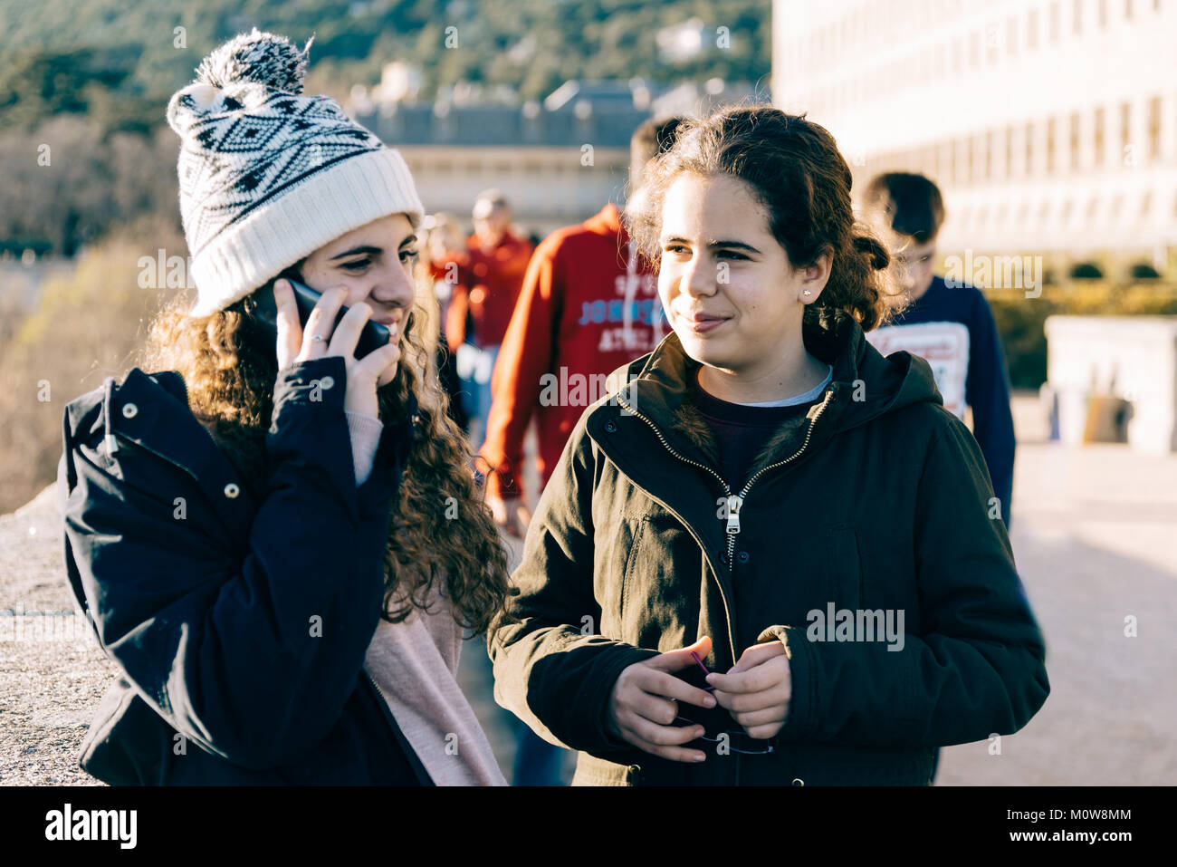 Felice ragazze adolescenti su di essi in knit hat texting con un telefono cellulare in un punto di riferimento. Concetto stare insieme Foto Stock