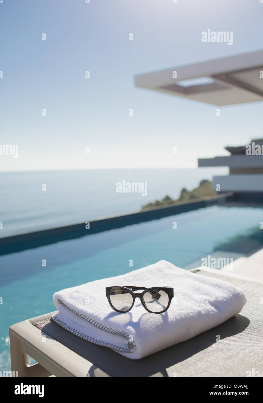 Occhiali da sole sulla Salvietta ripiegata a bordo piscina sul soleggiato patio di lusso con vista oceano Foto Stock
