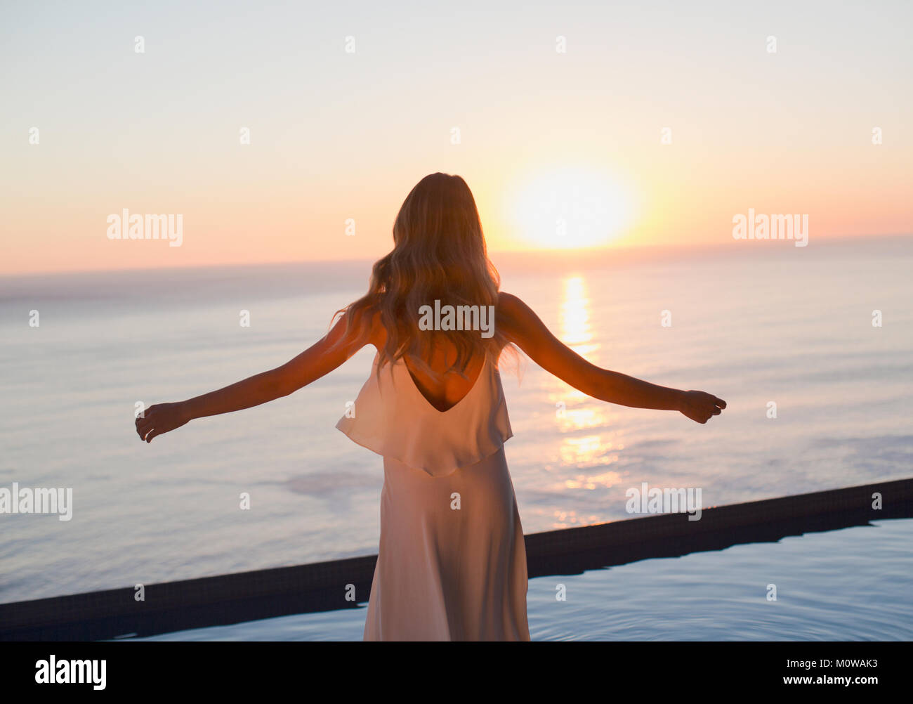 Donna con braccia tese a guardare tranquilla vista tramonto sull'oceano orizzonte Foto Stock