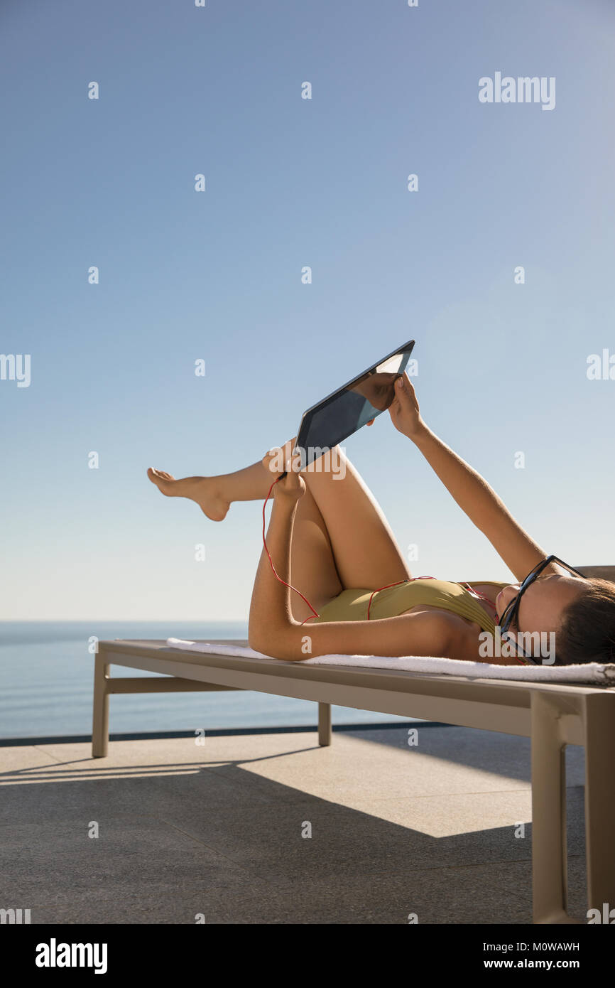La donna a prendere il sole, con tavoletta digitale sulla sedia a sdraio sul patio soleggiato Foto Stock