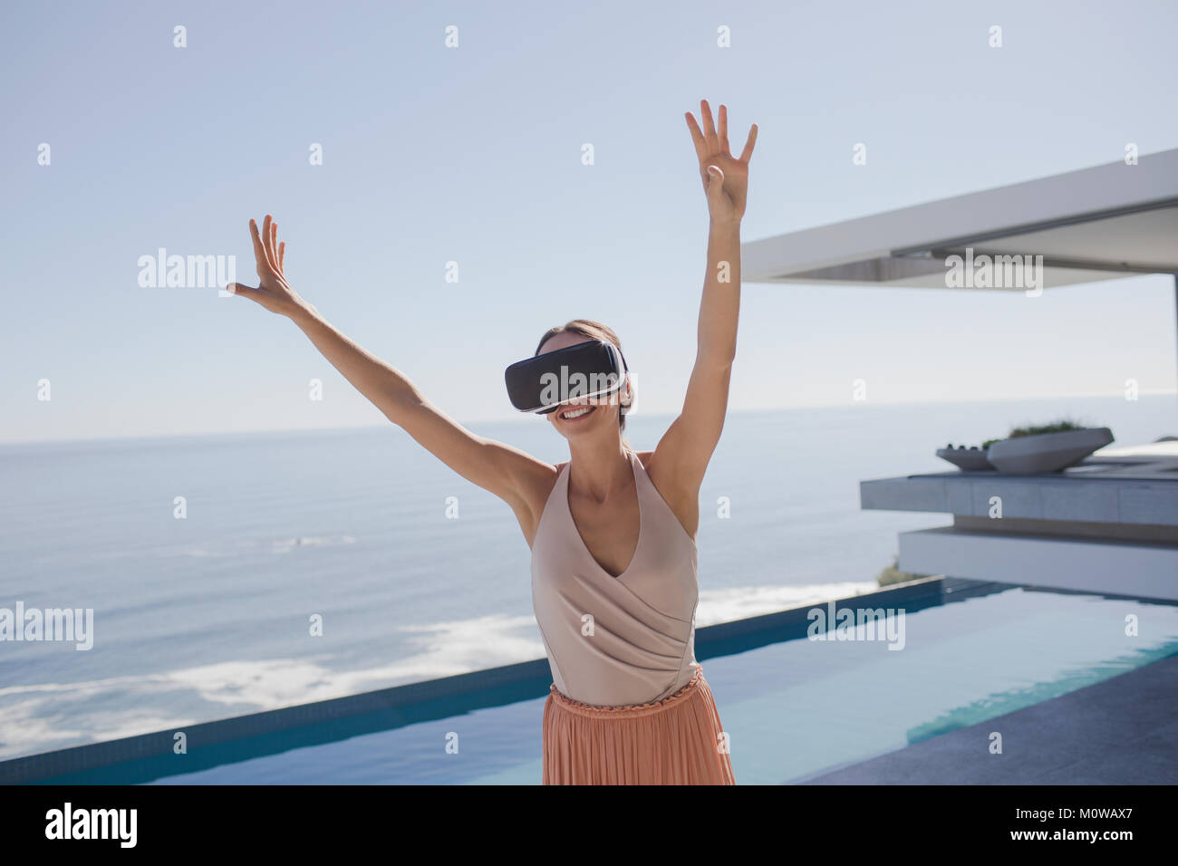 Donna energica utilizzando la realtà virtuale occhiali simulatore sulle moderne, lusso home vetrina patio esterno con vista oceano Foto Stock