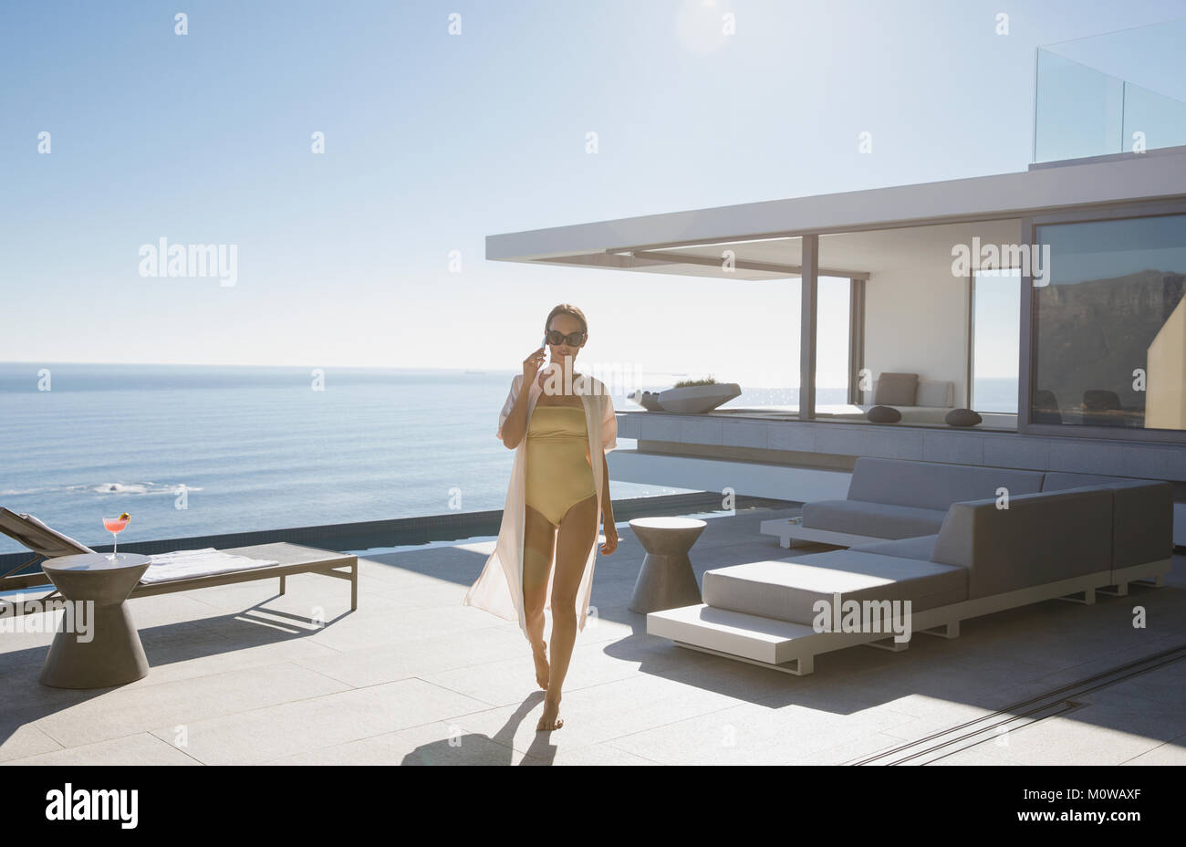 Donna in costume da bagno camminando sul soleggiato, moderno luxury home vetrina patio esterno con vista oceano Foto Stock