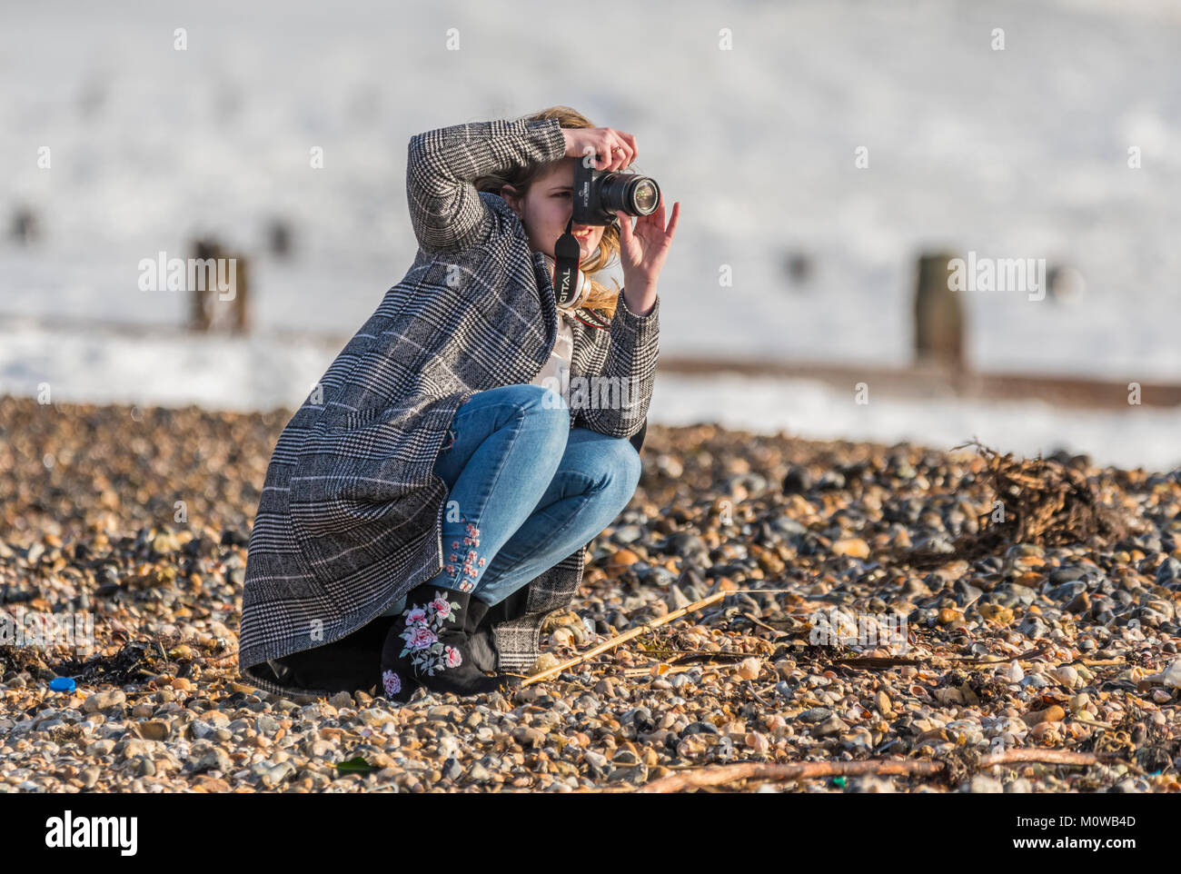Donna giovane fotografo femminile accovacciato in basso per scattare delle foto su una spiaggia. Foto Stock