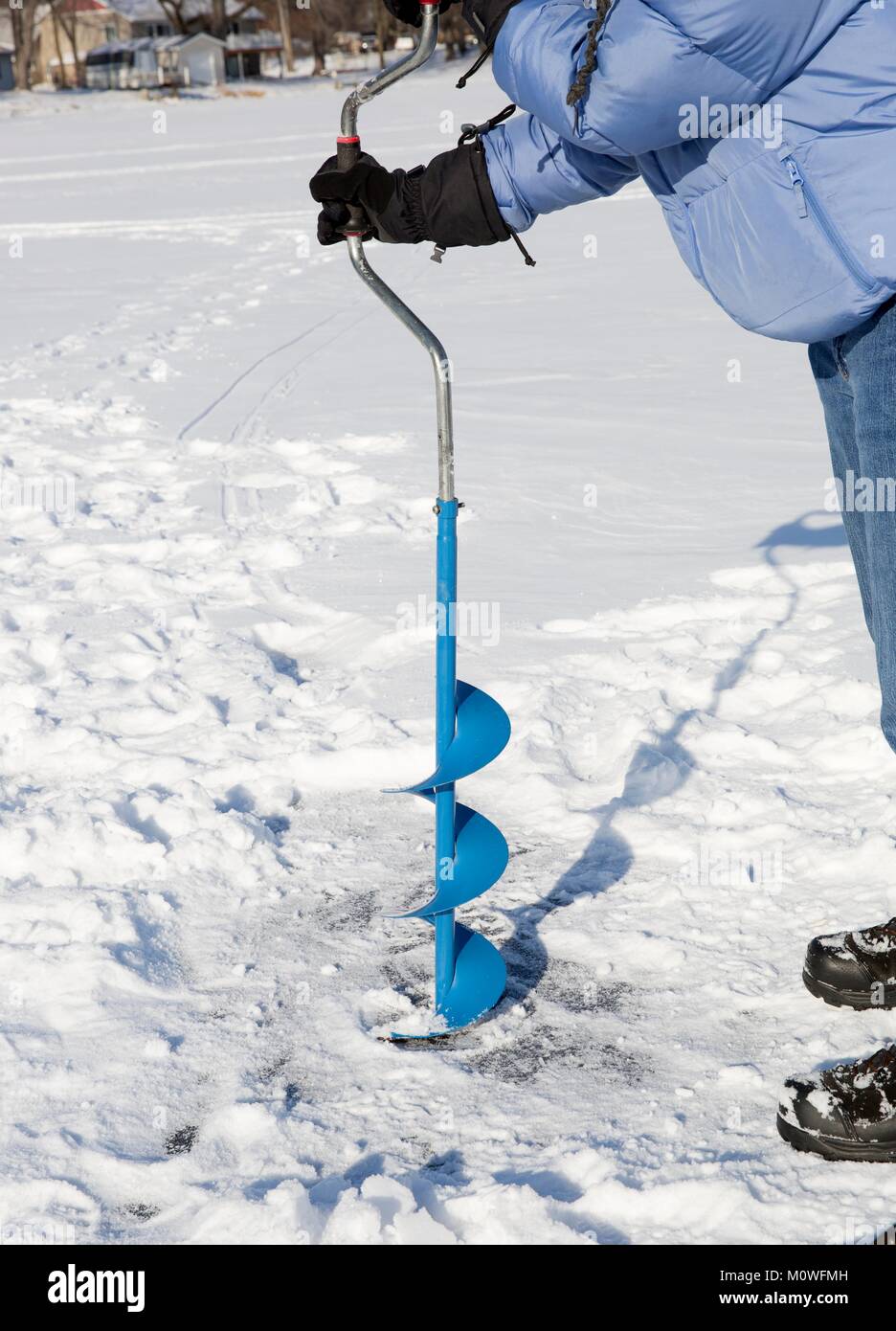 Una persona di praticare un foro nel ghiaccio di un lago ghiacciato usando un ice auguer (una vite elicoidale lama). Foto Stock