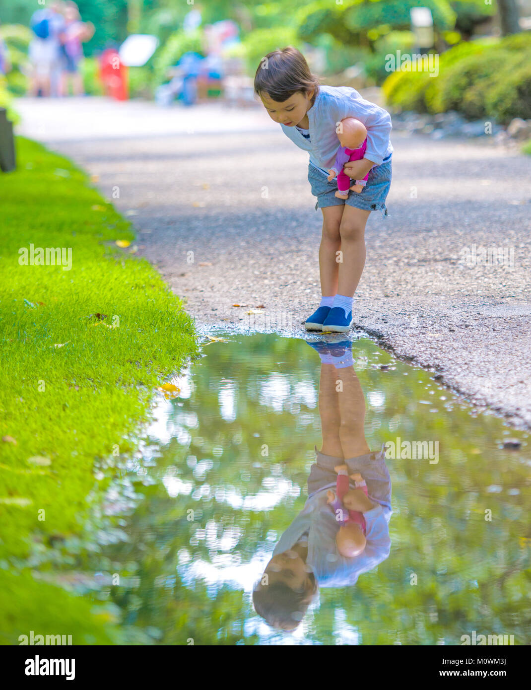 Bambina guarda in una pozza come uno specchio Foto Stock