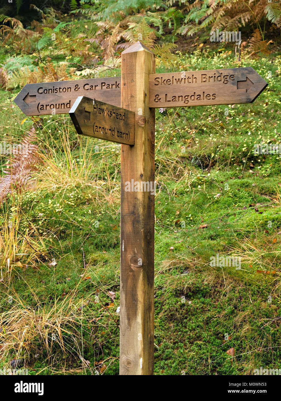 Dito di legno sentiero post segno indicante le direzioni per Skelwith Bridge, Langdales, Hawkshead e Coniston, Lake District inglese, Cumbria, England, Regno Unito Foto Stock