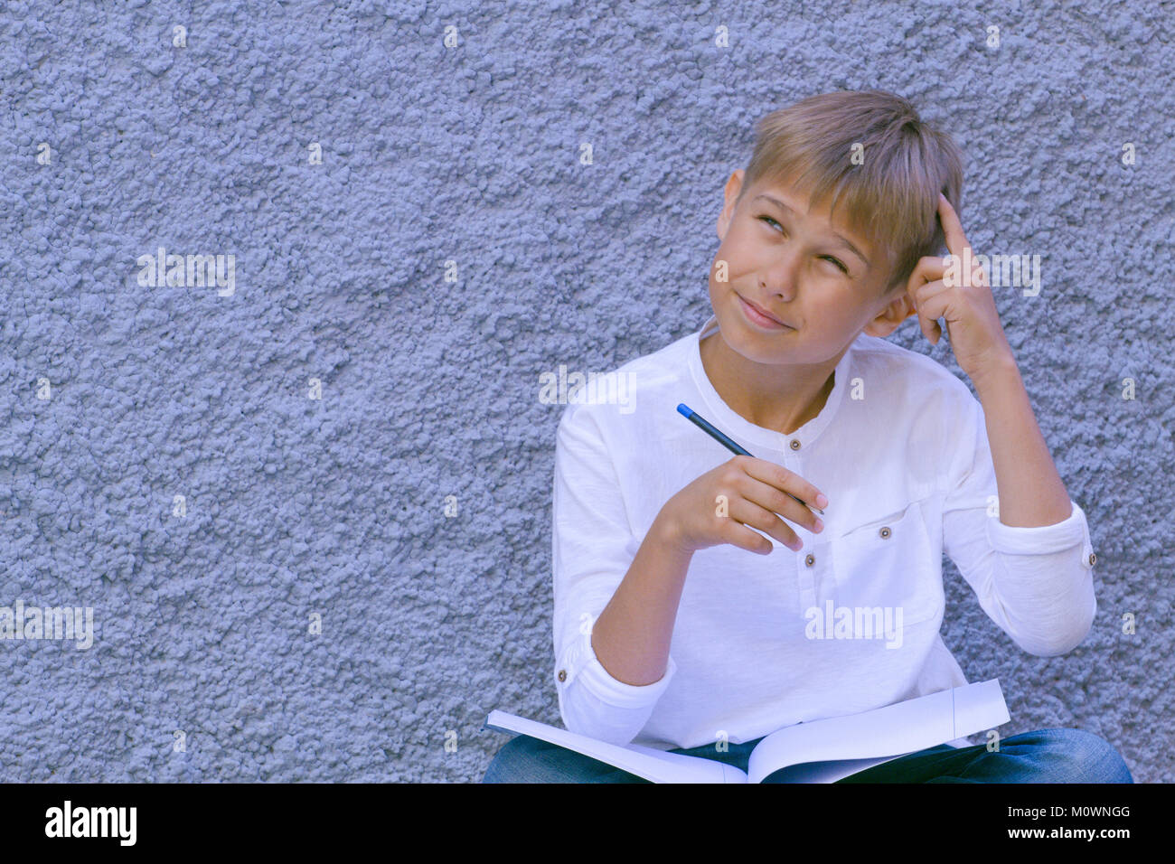 Il pensiero del ragazzo con un dito sulla fronte. Ragazzo seduto per terra e facendo i compiti di scuola. Foto Stock
