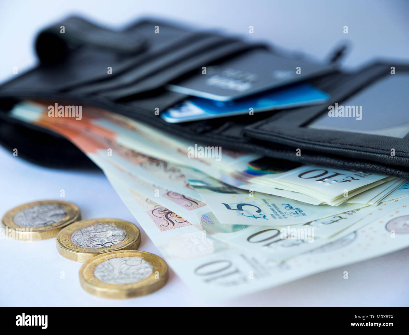 Un portafoglio nero contenente carte di credito o di debito e cinque e dieci pound note ventaglio con tre pound monete presso la parte anteriore Foto Stock