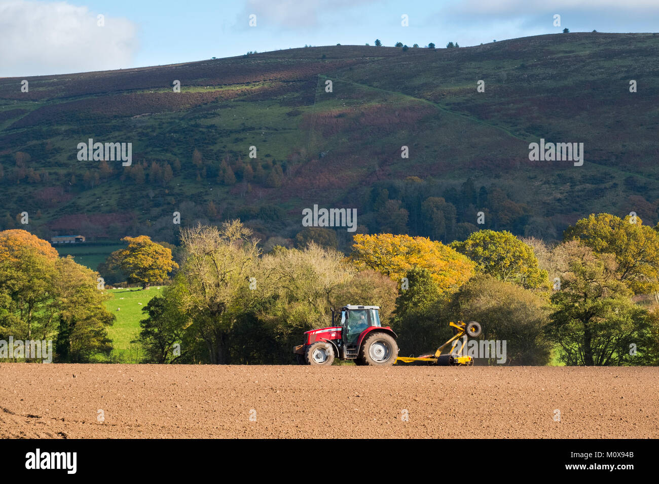 Un trattore agricolo lavorando in un campo sotto la lunga Mynd a Myndtown in Shropshire Hills, England, Regno Unito Foto Stock