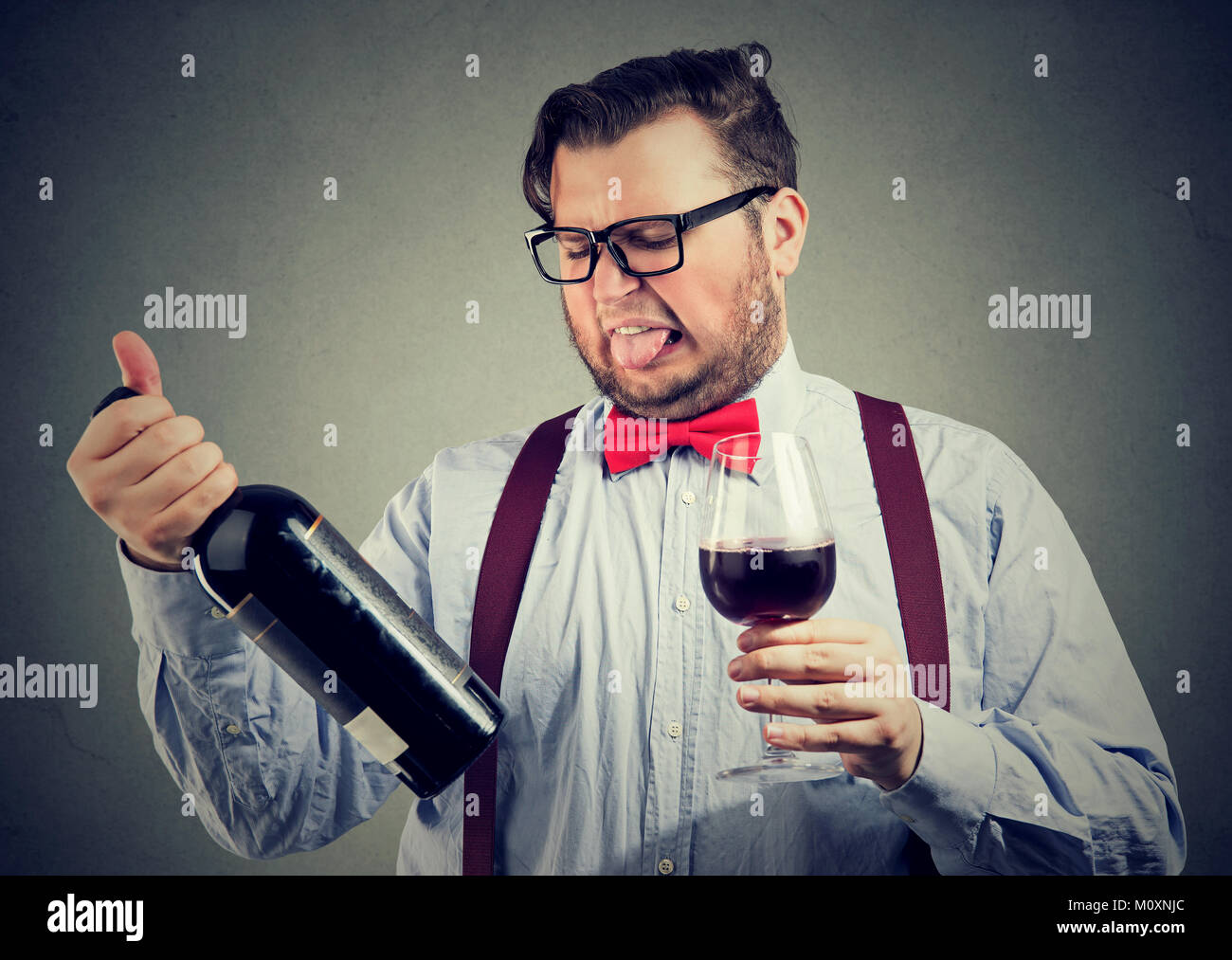 Uomo in bowtie cercando vino e cercando insoddisfatto mentre esplorate la bottiglia. Foto Stock