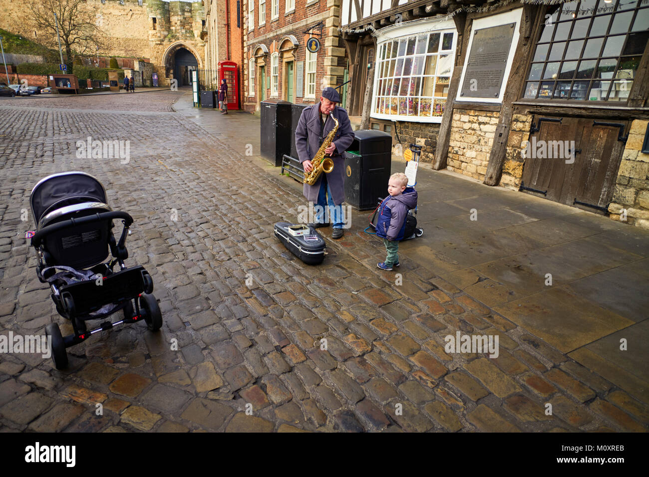 Un piccolo bambino perplesso incontra un uomo giocando un sassofono in strada a Lincoln Foto Stock