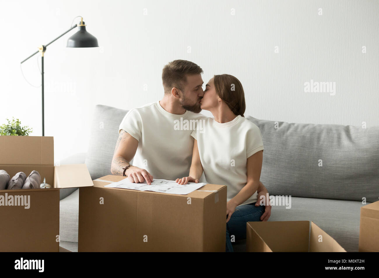 Felice nuovi proprietari di casa baciare sul divano in movimento in casa Foto Stock