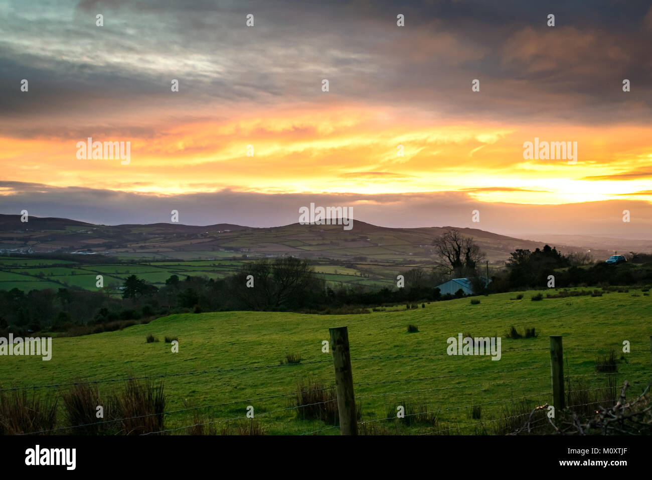 Oltre alla ricerca di un campo irlandese con montagne in lontananza e un tramonto dorato riflette le nuvole. Foto Stock