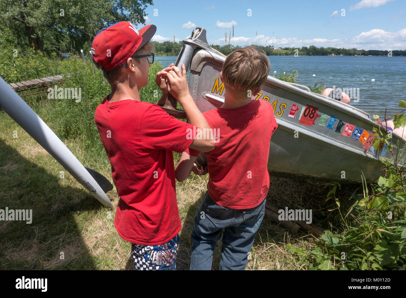Fratelli tirando il loro fine dell'alluminio barca da pesca al di fuori dell'acqua attraverso intonso impollinatrice erbacce dal lago Clitherall Minnesota MN USA Foto Stock