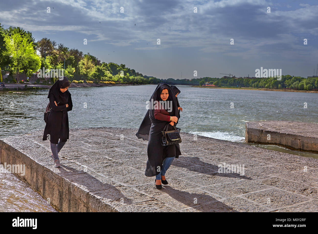 Isfahan, Iran - 24 Aprile 2017: tre donne sconosciuti in un nero velo religioso passeggiata lungo il fiume Zayandeh. Foto Stock