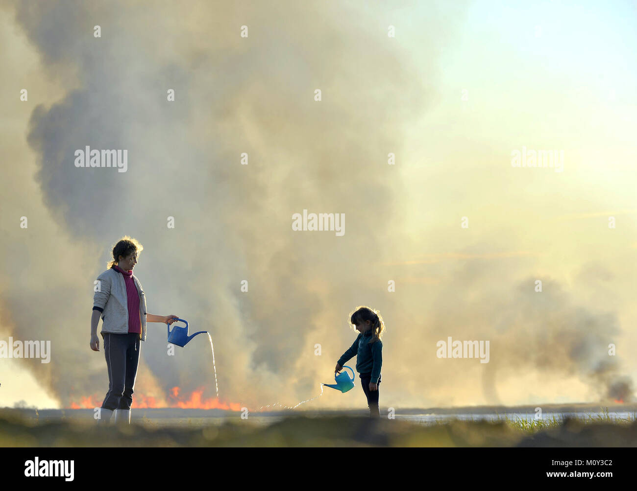 Madre e figlia piccola estinguere l'incendio dall'annaffiatoio. La masterizzazione di reed sulla riva del lago, wildfire Foto Stock