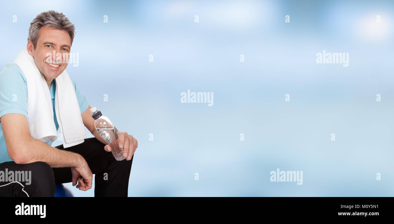 Ritratto di sorridente uomo Fitness tenendo la bottiglia di acqua contro il cielo blu Foto Stock