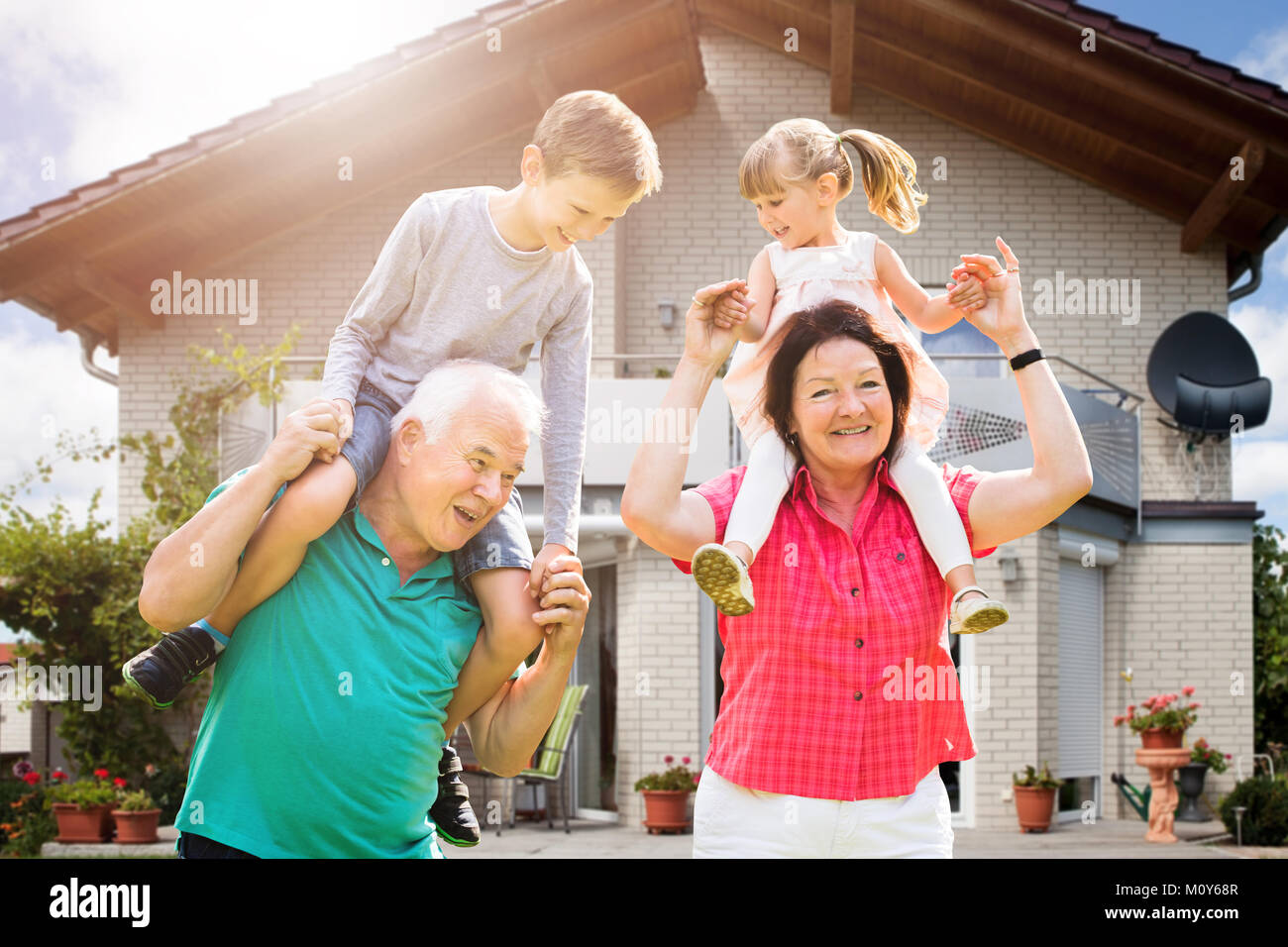 Sorridente nipoti è seduta sul nonno spalla godendo al di fuori della loro casa Foto Stock