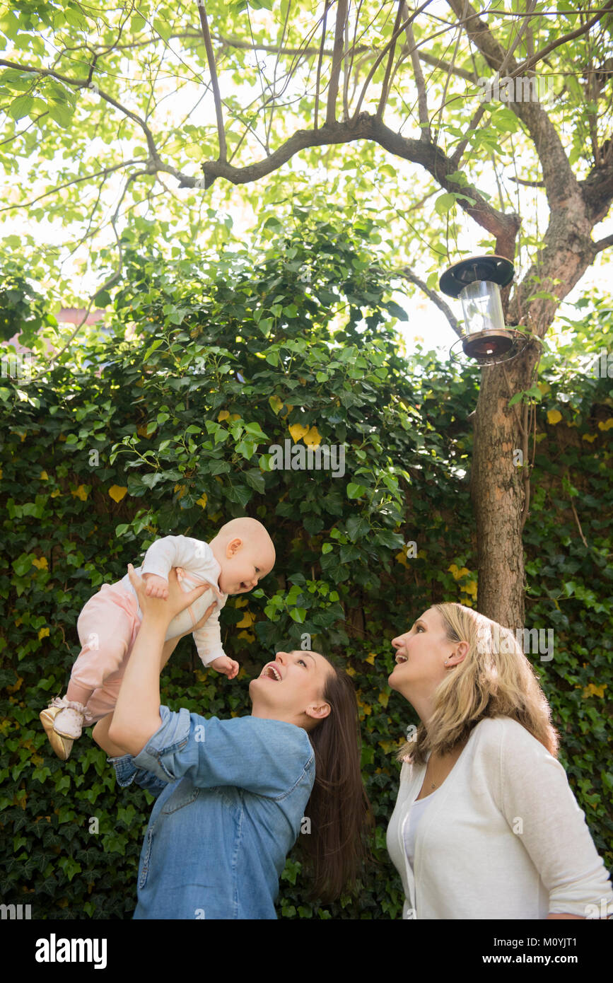 Le madri caucasica sollevamento figlia bambino sotto agli alberi Foto Stock