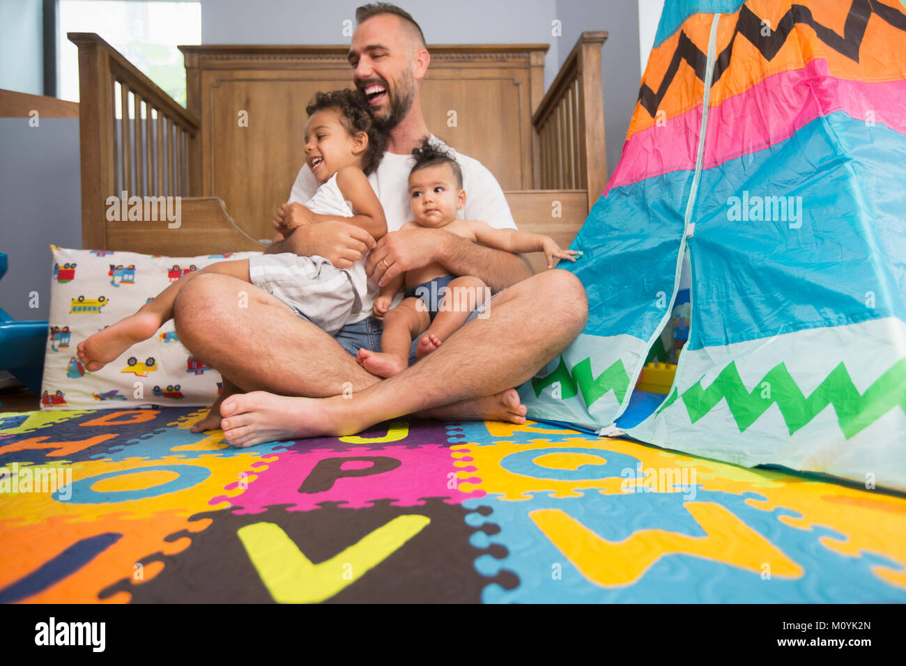 Padre seduto sul pavimento della sala giochi holding figlio e figlia Foto Stock