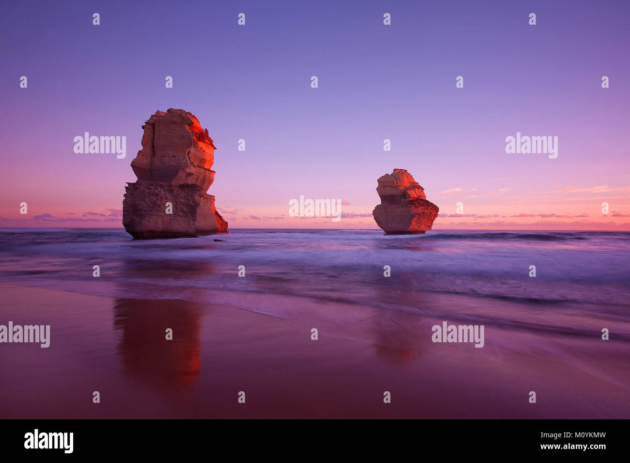 I Dodici Apostoli brillano nell'ultima luce del tramonto mentre le onde si infrangono sulla spiaggia lungo la costa frastagliata della Great Ocean Road nel Victoria, Australia. Foto Stock