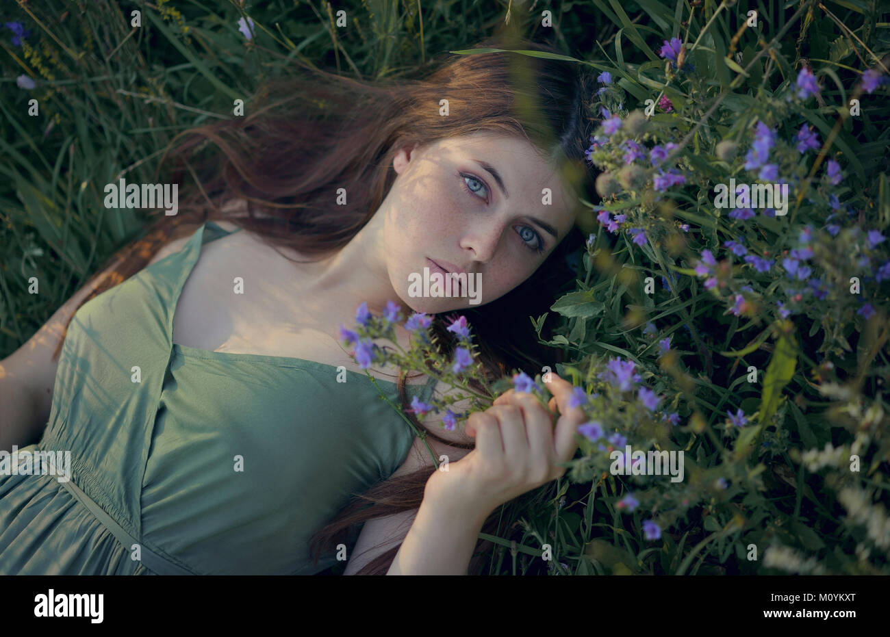 La donna caucasica posa in erba con fiori di campo Foto Stock