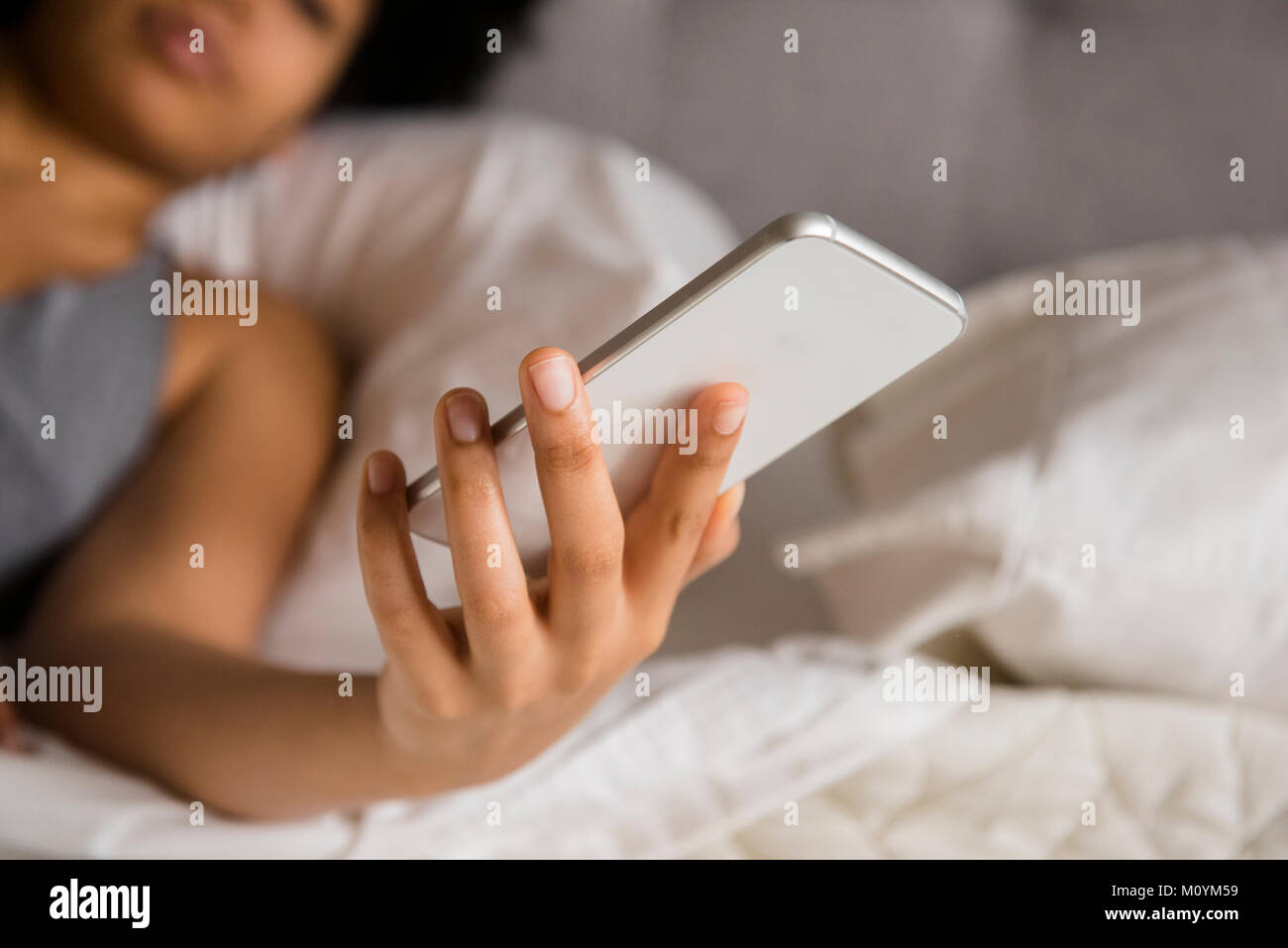 African American donna posa sul letto gli sms sul cellulare Foto Stock
