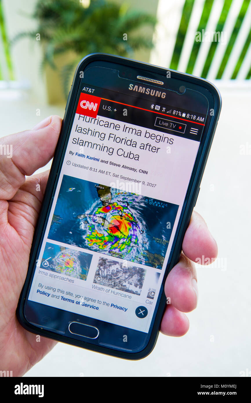 In seguito e monitoraggio di un uragano Irma di avvertimento sulla televisione e un cellulare tenuto in mano lo smartphone dispositivo Foto Stock