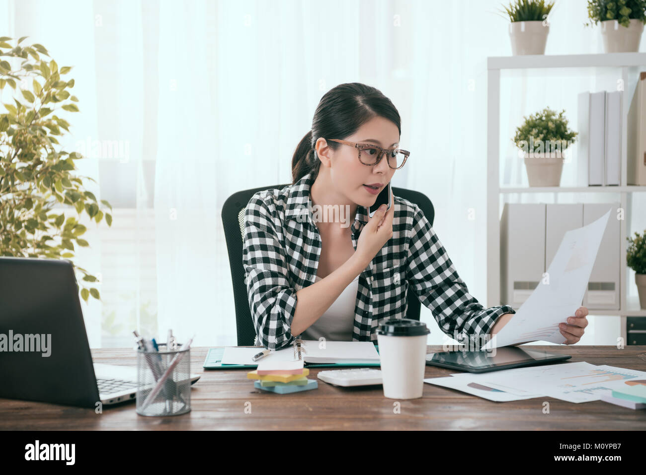 Elegante femmina attraente lavoratore di ufficio tramite telefono cellulare chiamando collega per discutere il piano di lavoro quando si lavora a casa e la navigazione compa Foto Stock