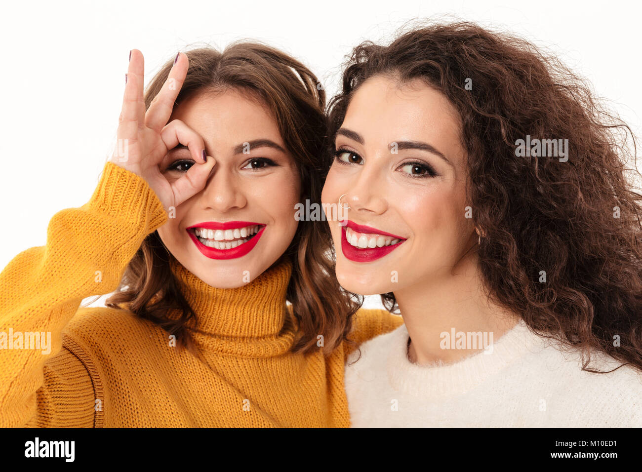 Chiudere l'immagine delle due ragazze felici in maglioni divertendosi e guardando la telecamera su sfondo bianco Foto Stock