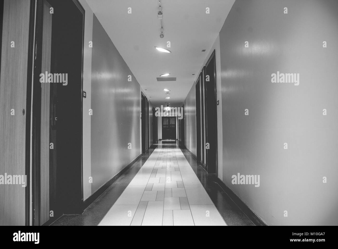 Immagine in bianco e nero di architettura lunga passerella o sentiero all'interno di edificio fiancheggiato con porta di legno e muro. Foto Stock