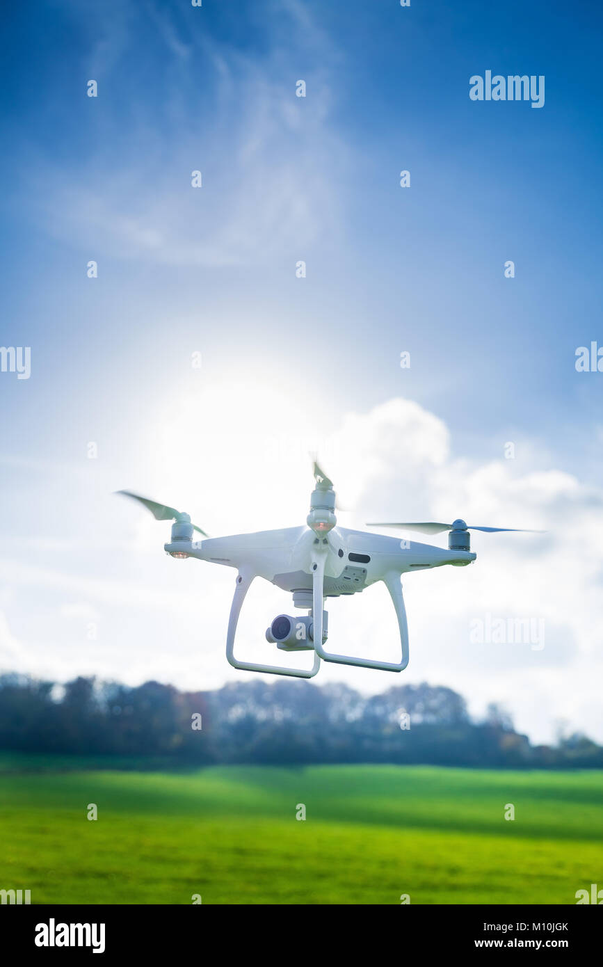 Foto di un flying bianco quadcopter professionale drone fotocamera nella parte anteriore di erba verde e foresta Foto Stock